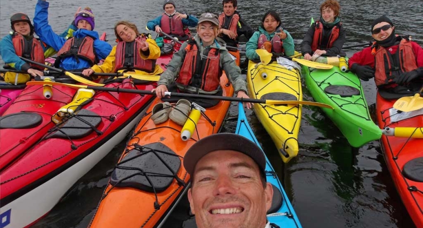 a group of people wearing life jackets sit in colorful kayaks bunched together and smile for the photo 